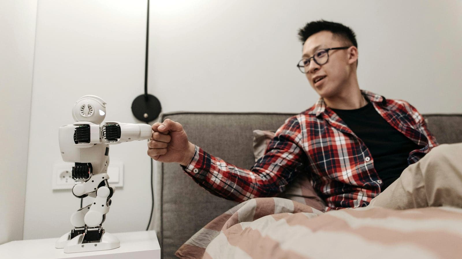 Junger Mann gibt einem kleinen humanoiden Roboter den Faustgruß — Mensch und KI auf Augenhöhe